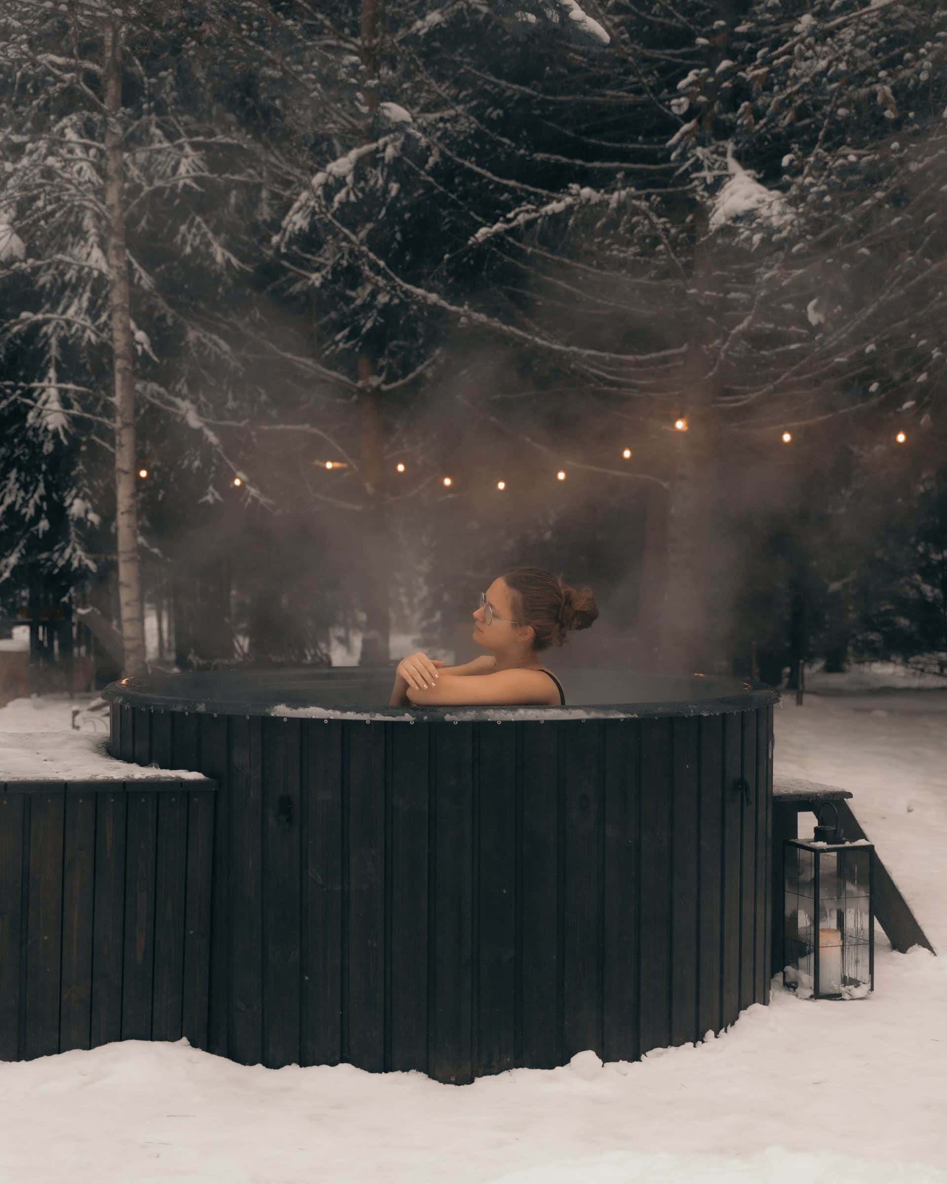 The hot tub in winter — snow firs, string lights, lantern with candle
